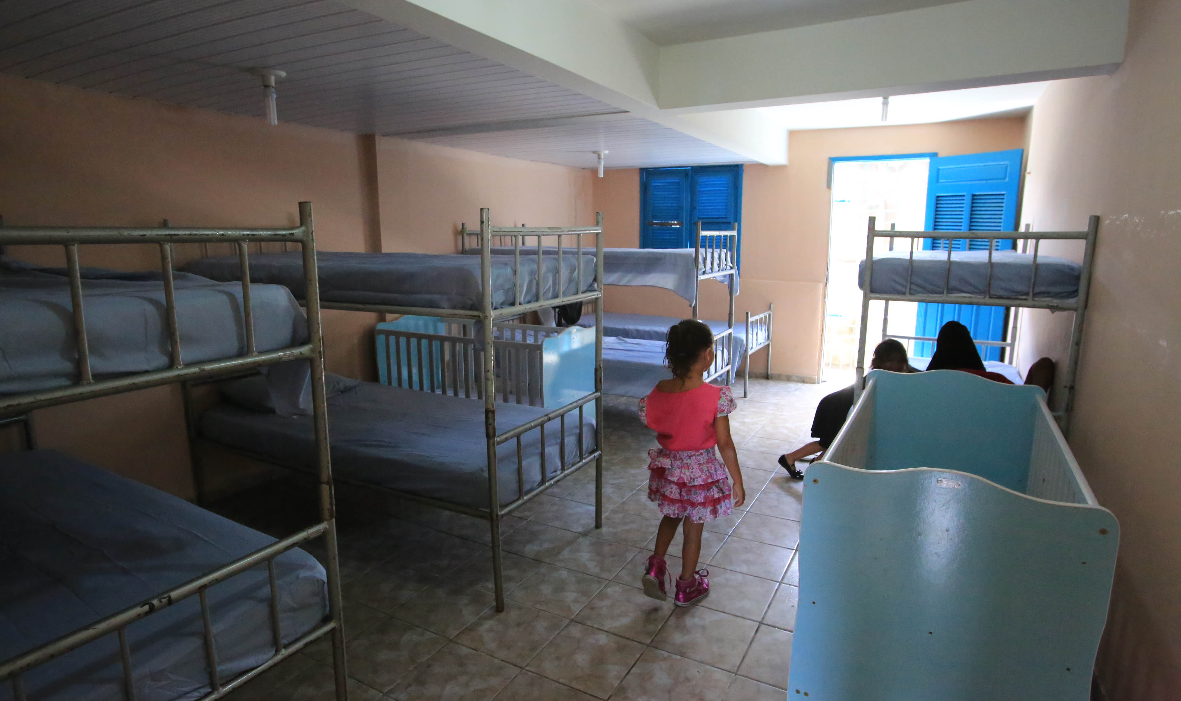 uma criança de costa caminha em um quarto com quatro camas beliche